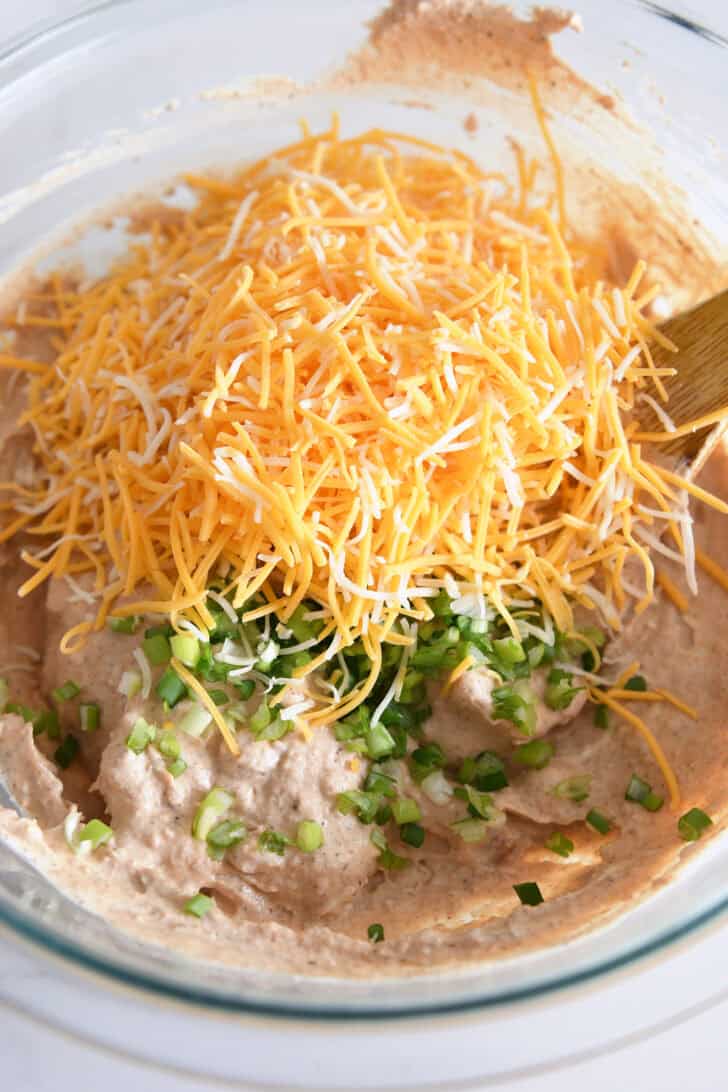 Creamy refried bean mixture in bowl with shredded cheese and green onions.
