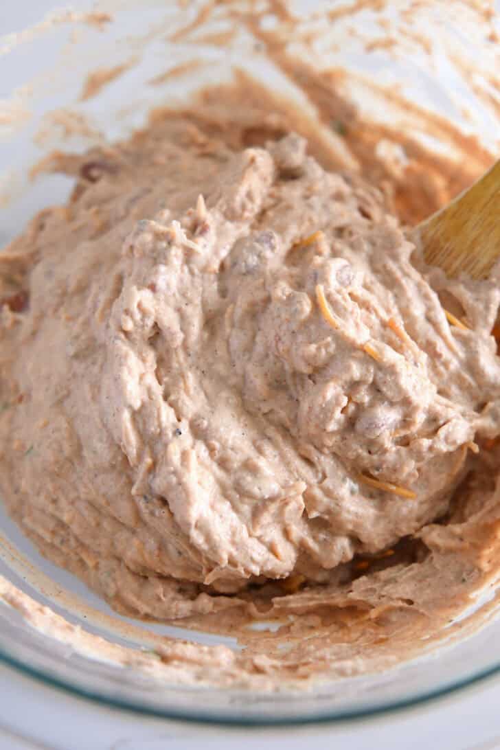 Refried beans, sour cream, cream cheese, and spices mixed together in glass bowl.