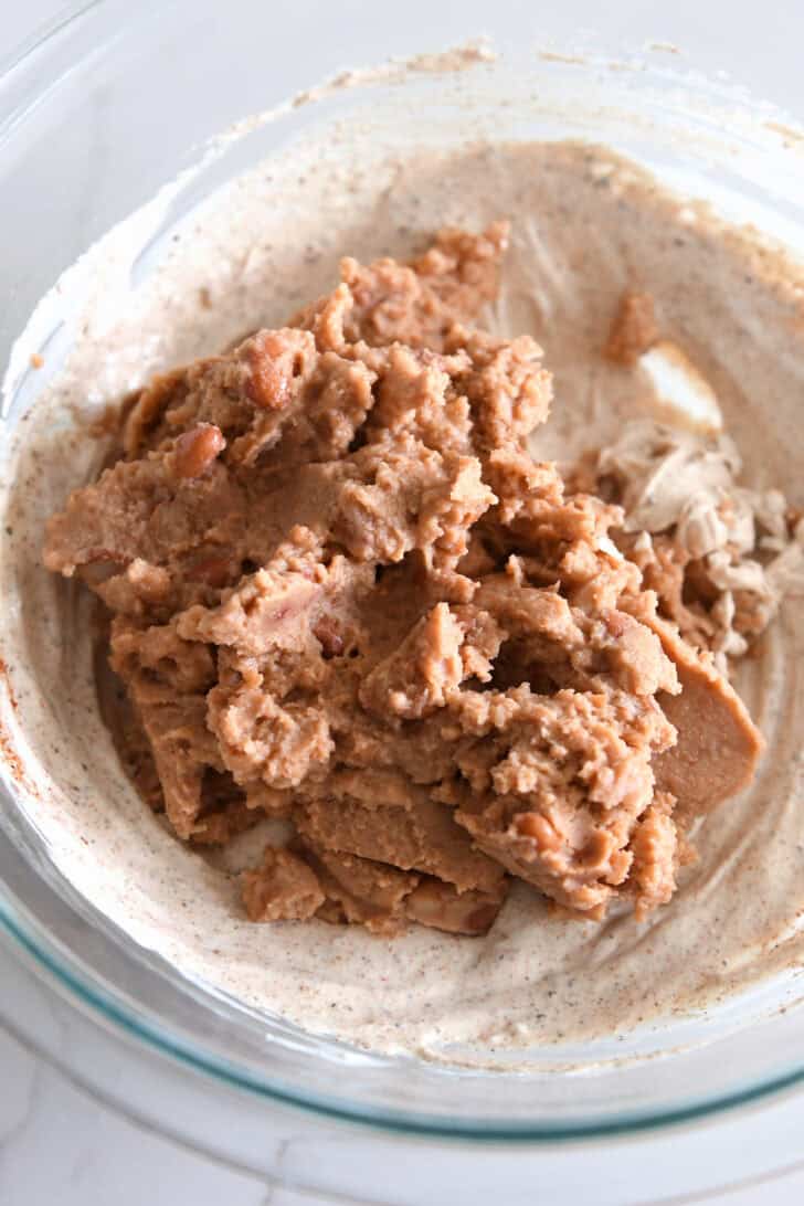 Refried beans in bowl with creamy sour cream and spice mixture.