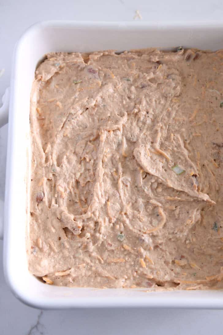 White square baking pan with creamy refried bean dip spread evenly.