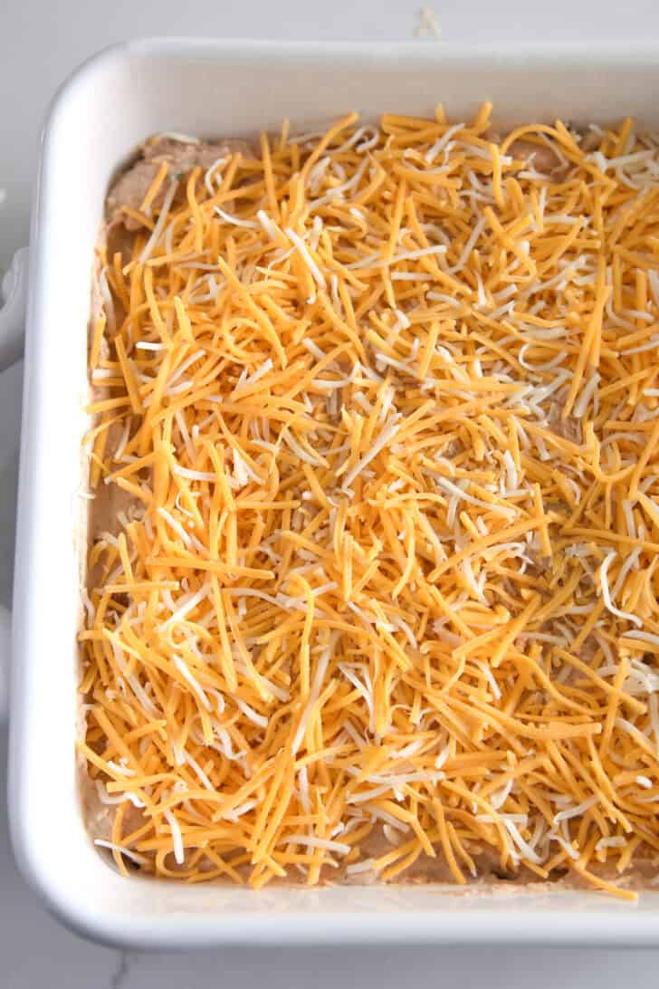 White square baking pan with bean dip and shredded cheese.
