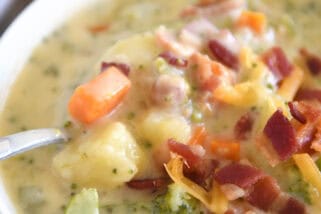 Spoon scooping spoonful of loaded broccoli cheese bacon soup in white bowl.