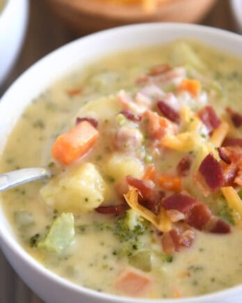 Spoon scooping spoonful of loaded broccoli cheese bacon soup in white bowl.