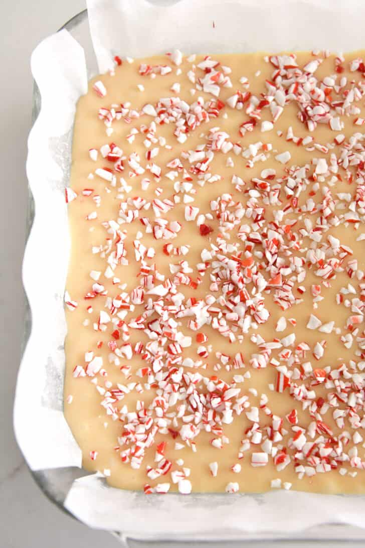 Top down view of white chocolate fudge and peppermint pieces in parchment-lined baking pan.
