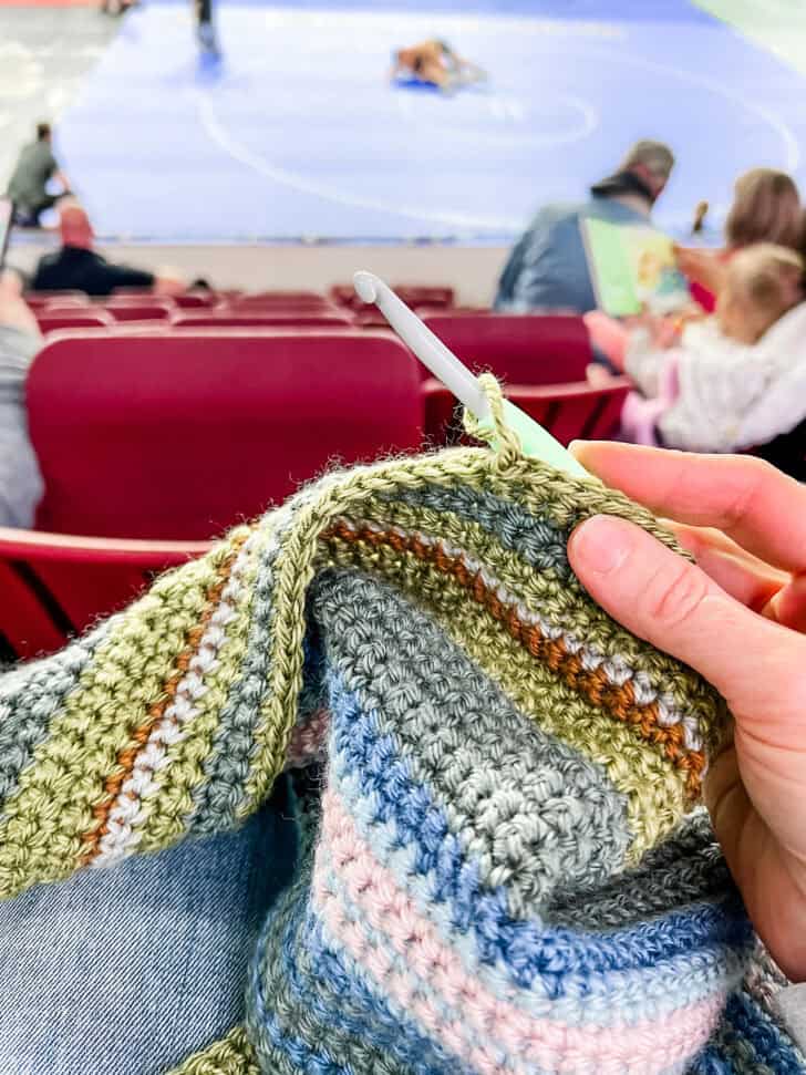 Crocheting green stripes on temperature blanket.