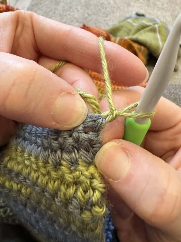 Crocheting first stitch in second row of temperature blanket.