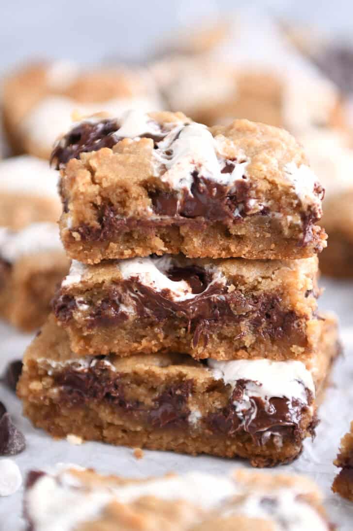 Three s'mores cookie bars stacked on top of each other on a piece of parchment paper.