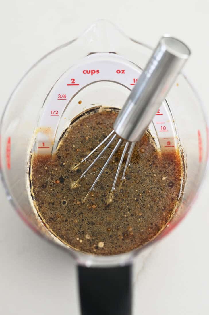 Top down view of liquid measuring cup with small whisk, soy sauce, and brown sugar.