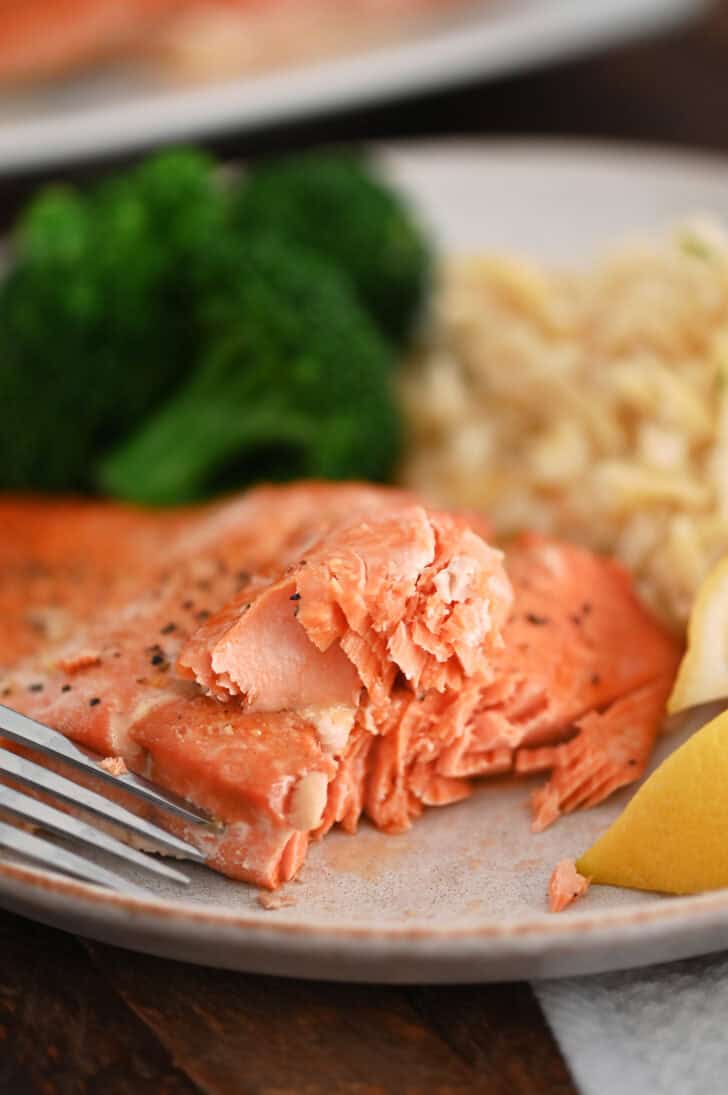 Salmon on gray plate with fork, rice pilaf and cooked broccoli.