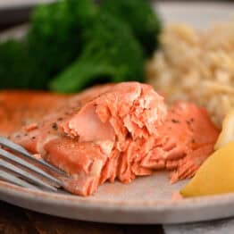 Salmon on gray plate with fork, lemon wedges, cooked broccoli and rice pilaf.