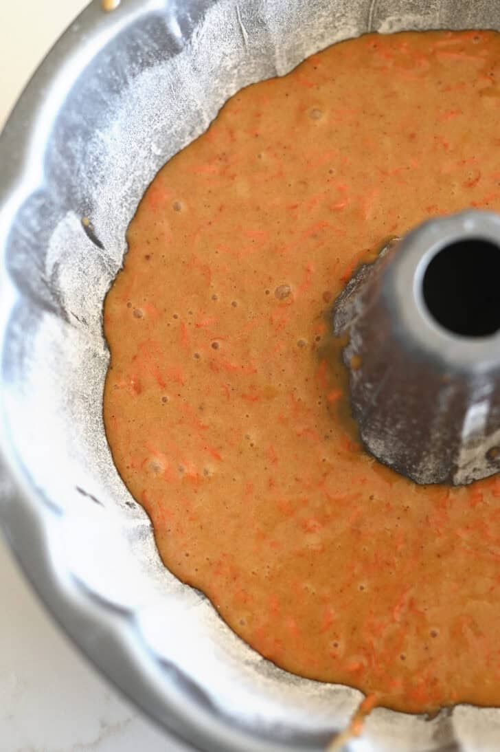 Top down view of a greased and floured metal bundt pan with raw carrot cake batter inside.