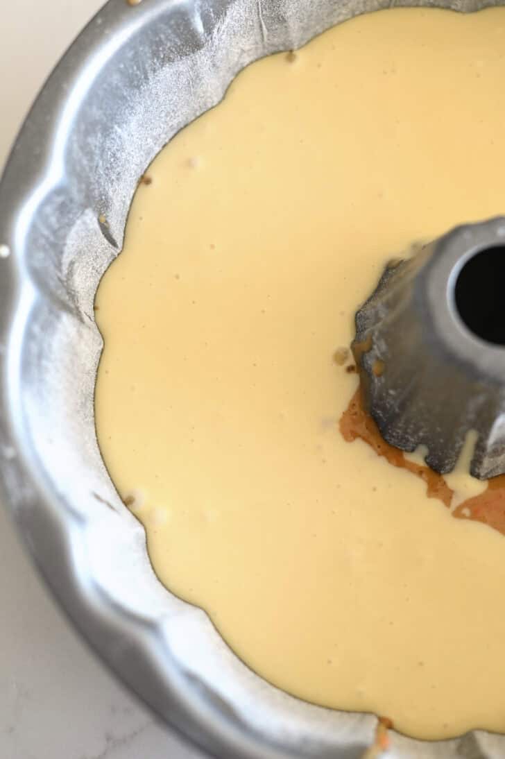 Top down view of a greased and floured bundt cake pan with a raw carrot cake and cream cheese batter.