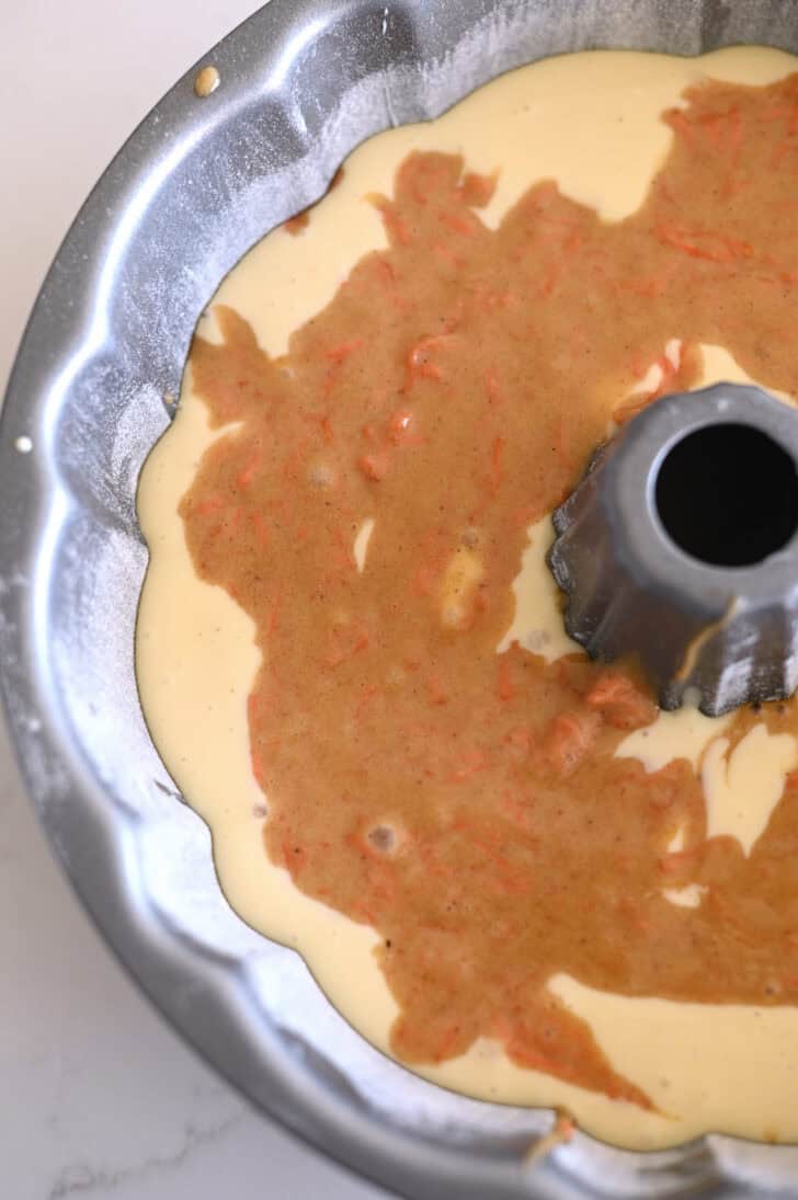 Top down view of a greased and floured bundt cake pan with a raw carrot cake and cream cheese batter.