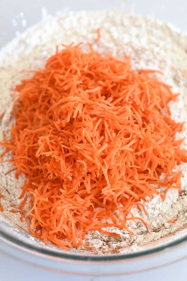 Top down view of a glass bowl with a carrot cake flour mixture and shredded carrots.