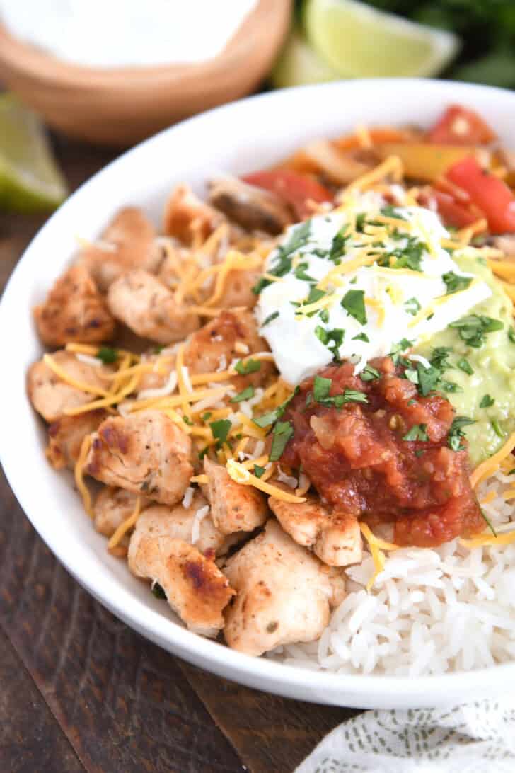 White shallow bowl with rice, grilled chicken, salsa, guacamole and sour cream.