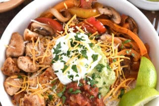 Top down view of rice, limes, grilled chicken, salsa, sour cream, guacamole, bell peppers and mushrooms.