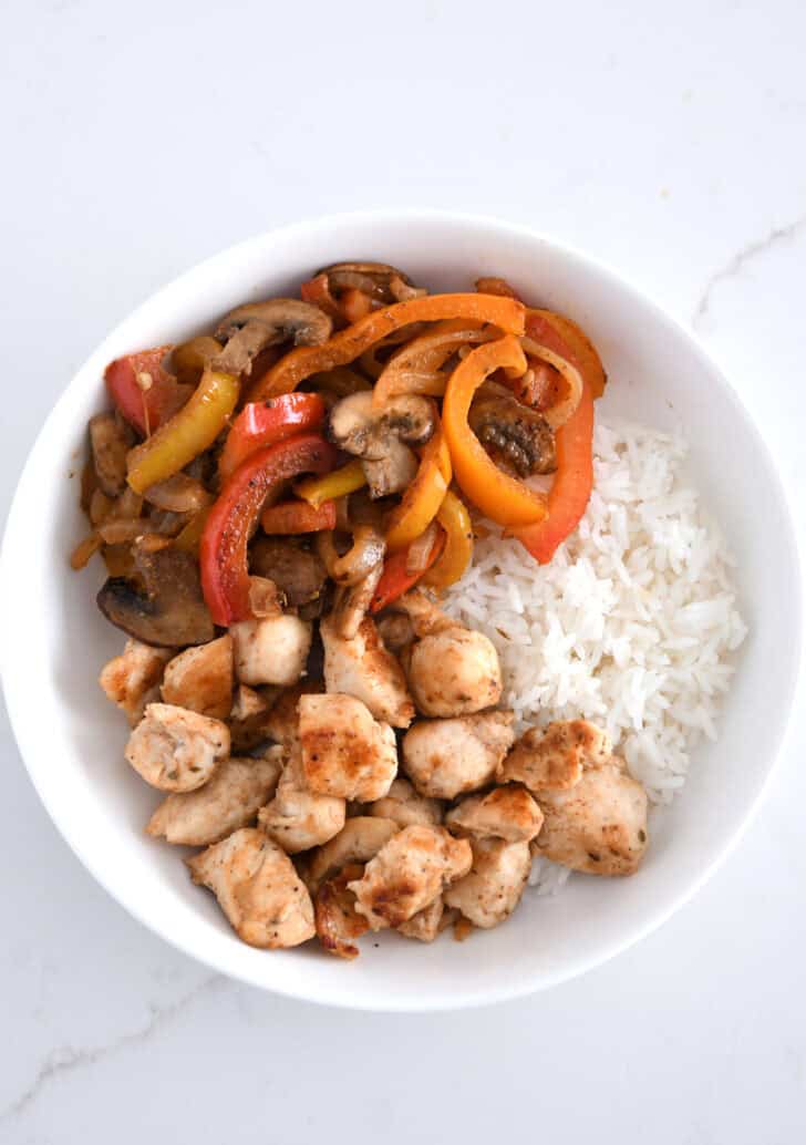 Top down view of white bowl with grilled chicken, rice, bell peppers, onions and mushrooms.