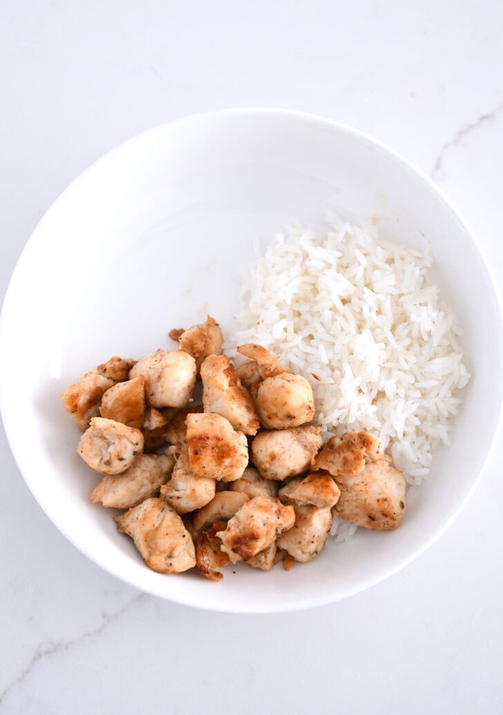 Top down view of white bowl with rice and grilled chicken.