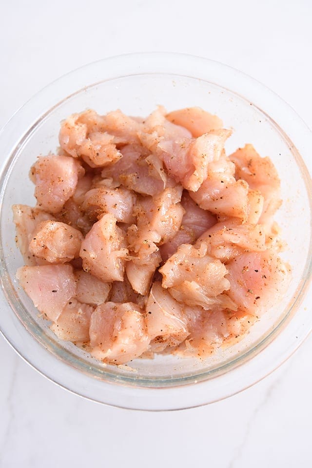 Top down view of glass bowl with chicken pieces seasoned with fajita seasoning.