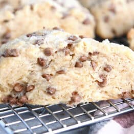 Side view of a baked cinnamon chip scone on a wire cooling rack with more scones behind it.