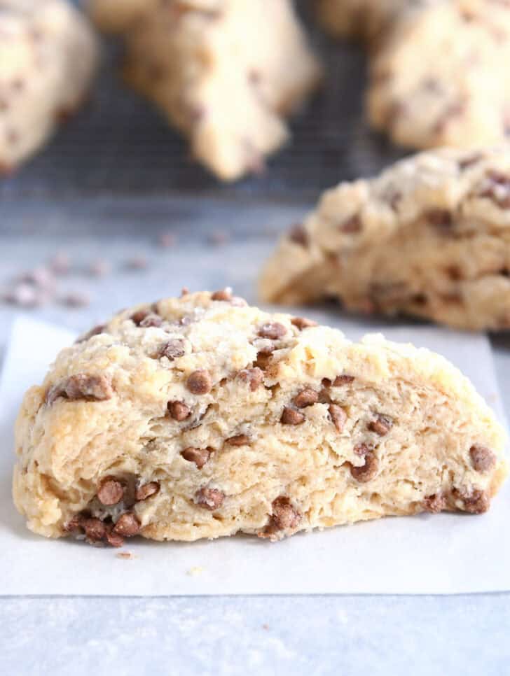Side view of a baked cinnamon chip scone on a piece of parchment paper with more scones behind it.