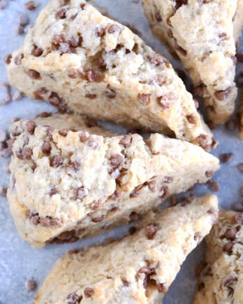 Top view of baked cinnamon chip scones with cinnamon chips sprinkled all around them on a piece of parchment.