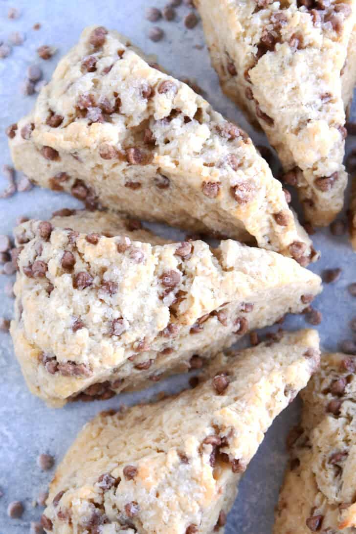 Top view of baked cinnamon chip scones with cinnamon chips sprinkled all around them on a piece of parchment.