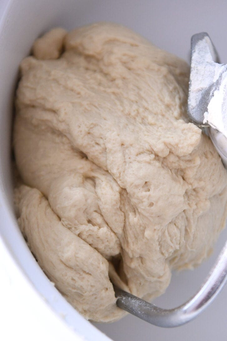 Top down view of the inside of a Bosch mixing bowl with a dough hook and a big ball of bread dough.