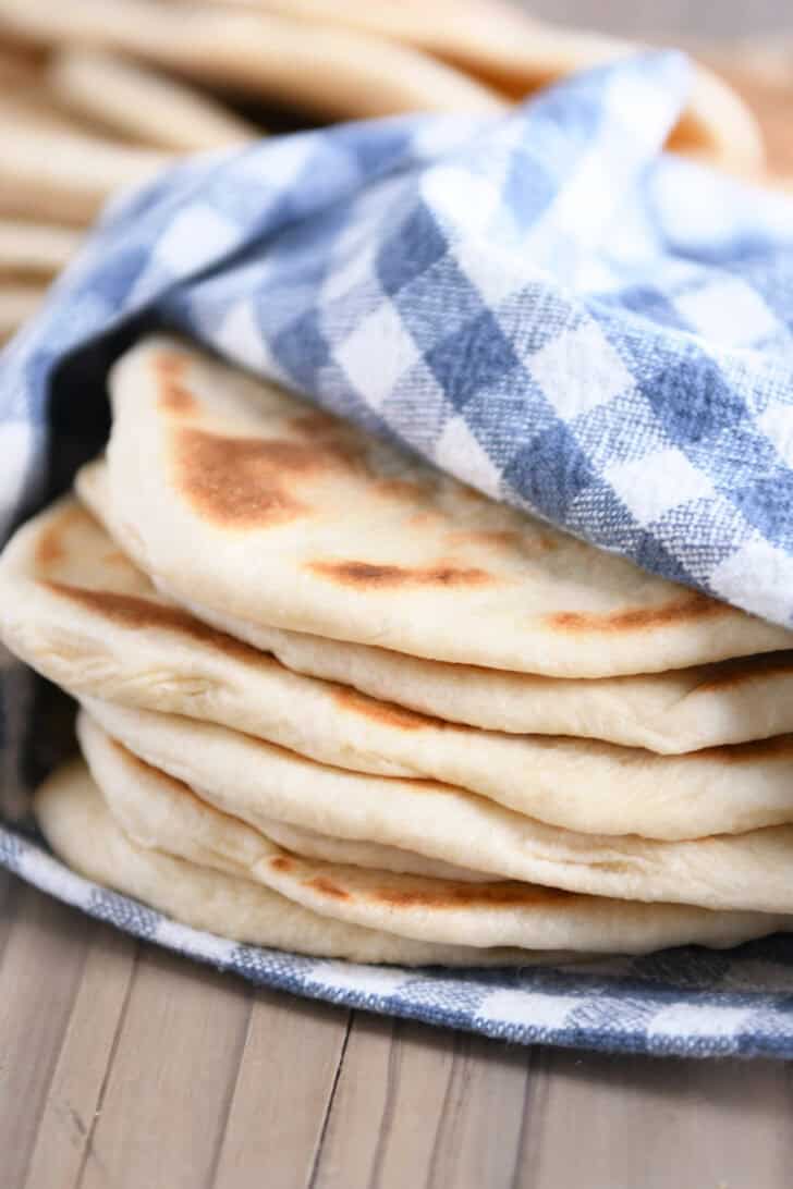 A stack of golden brown flatbreads wrapped in a blue and white checkered kitchen towel.