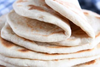 A stack of golden brown flatbread on a wooden cutting board. The top two flatbreads are folded in half.