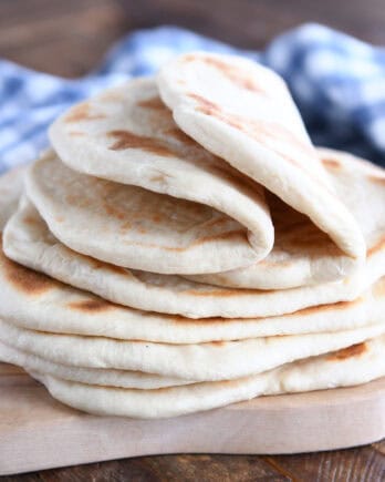 A stack of golden brown flatbread on a wooden cutting board. The top two flatbreads are folded in half.
