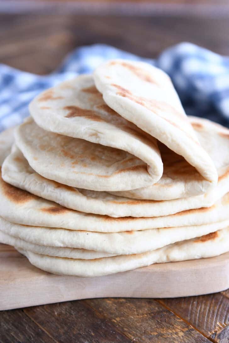 A stack of golden brown flatbread on a wooden cutting board. The top two flatbreads are folded in half.