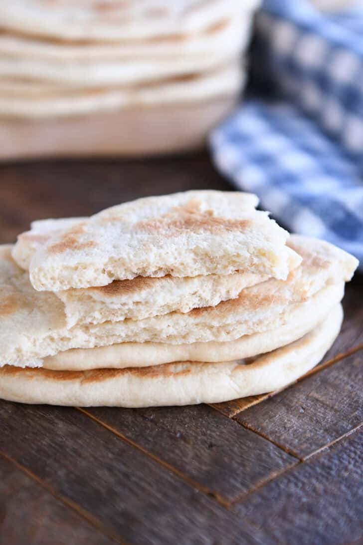 A stack of flatbread on a wooden counter. The top flatbread is torn into pieces.