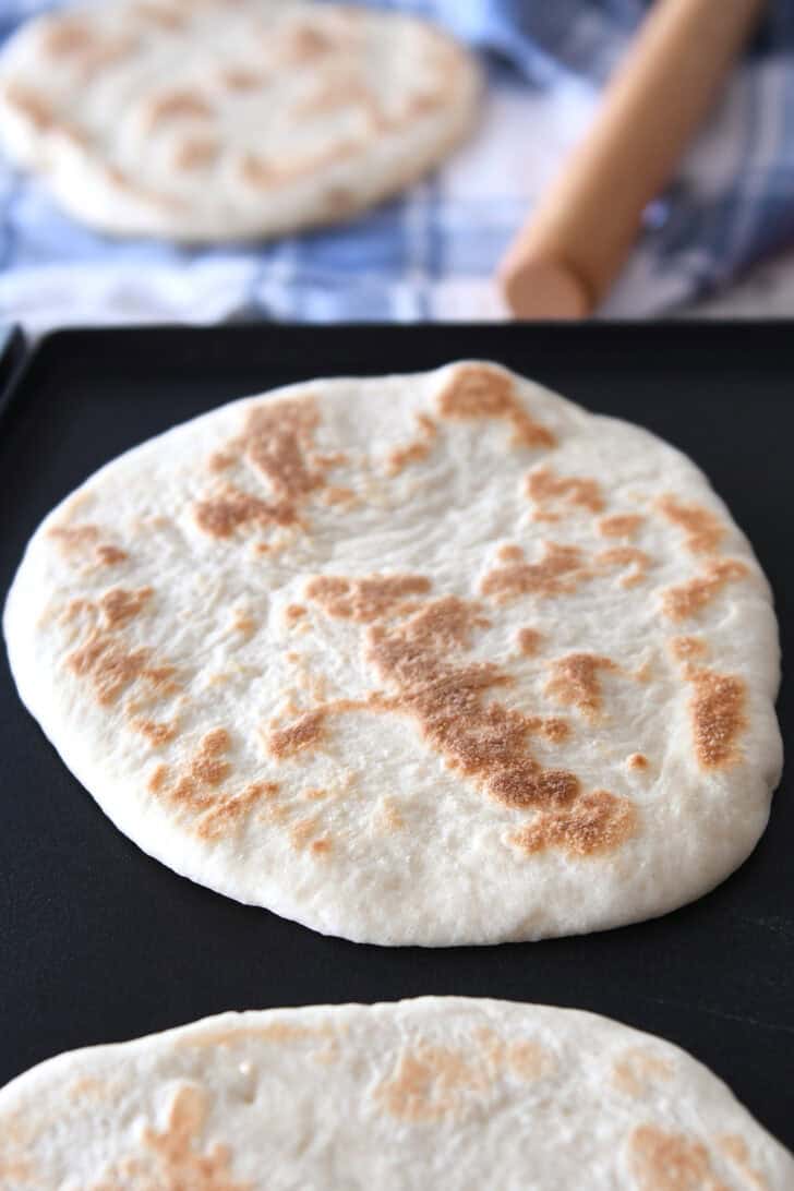 Golden brown round flatbreads getting cooked on a griddle.