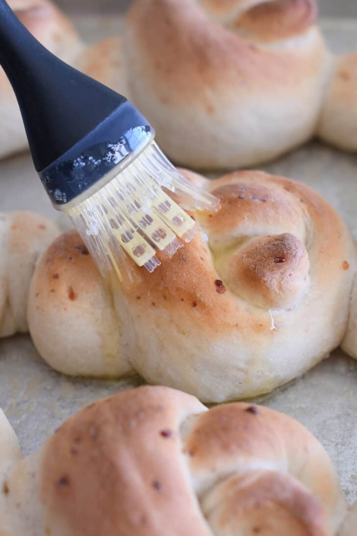 Brushing butter over the top of hot, baked parmesan breadstick knot.