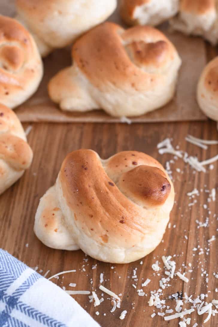 Parmesan breadstick knot with shredded Parmesan cheese and white and blue cloth on wood board.