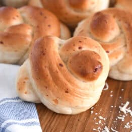Several baked breadstick knots on wood board with white and blue cloth.