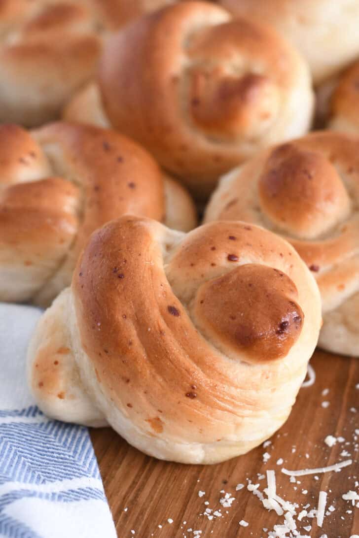 Several baked breadstick knots on wood board with white and blue cloth.