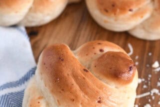 Several baked breadstick knots on wood board with white and blue cloth.