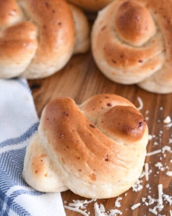 Several baked breadstick knots on wood board with white and blue cloth.