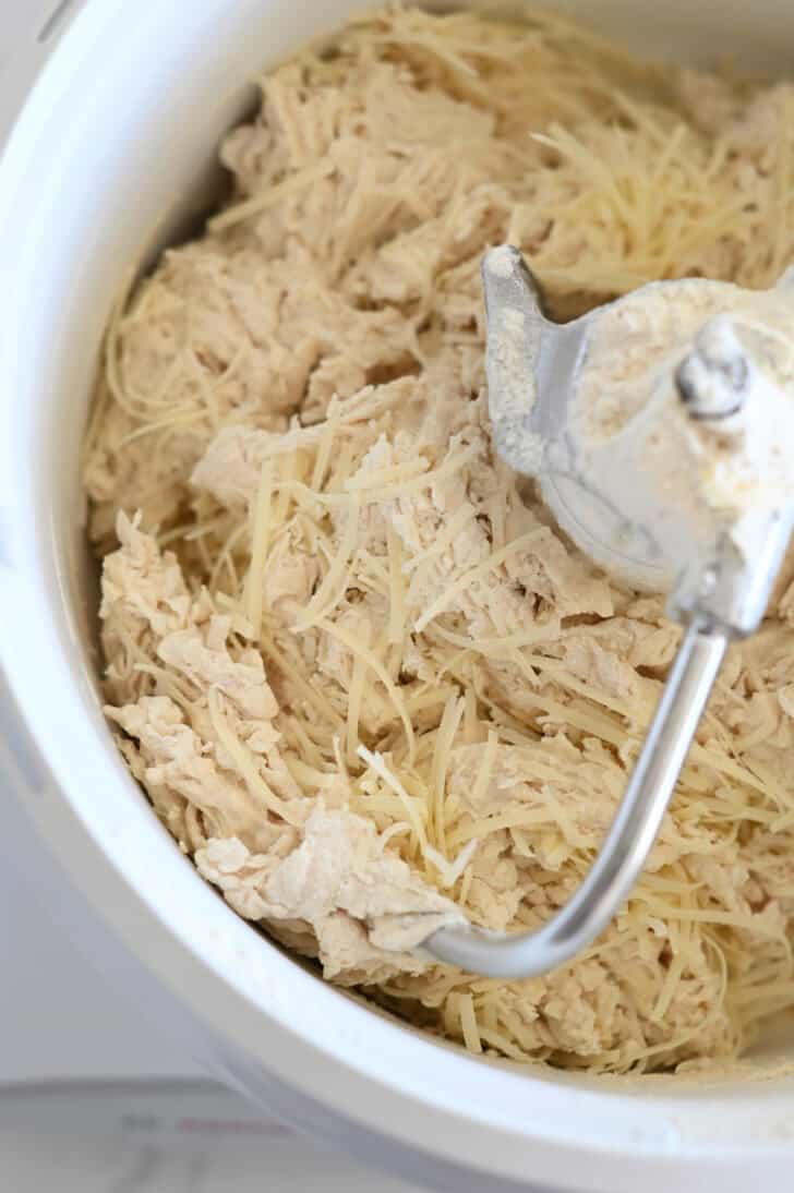 Freshly grated Parmesan cheese added to breadstick dough in white Bosch mixer with dough hook.