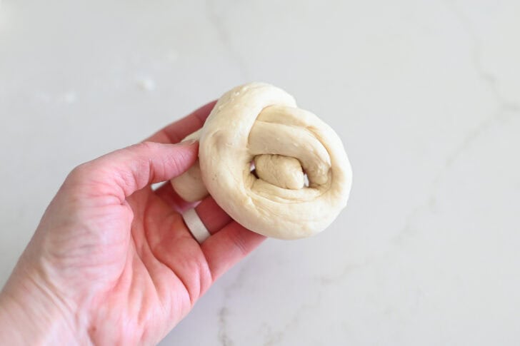 Bringing end of breadstick dough through hole to make breadstick knot.