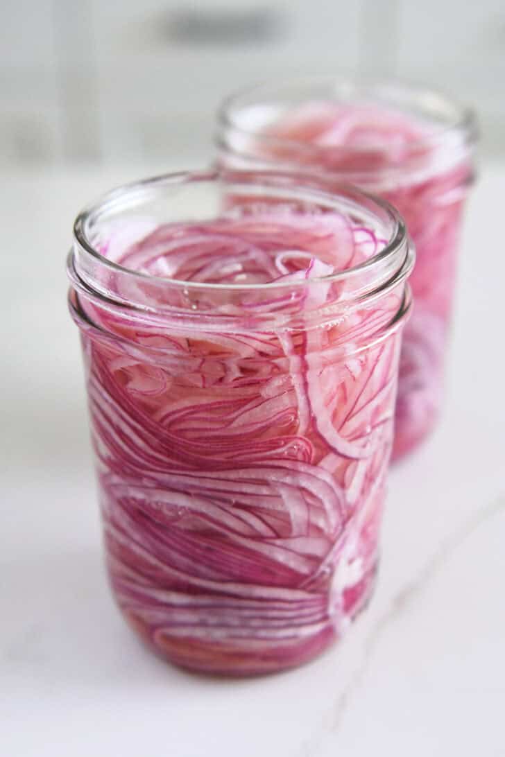 Two pint jars with thinly sliced red onions and vinegar.