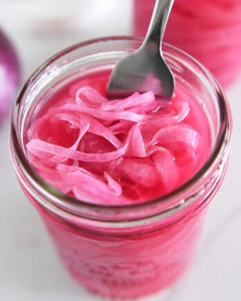 Top down view of fork in jar with pickled red onions.