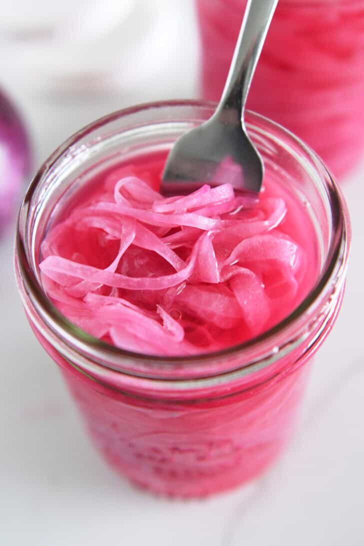 Top down view of fork in jar with pickled red onions.