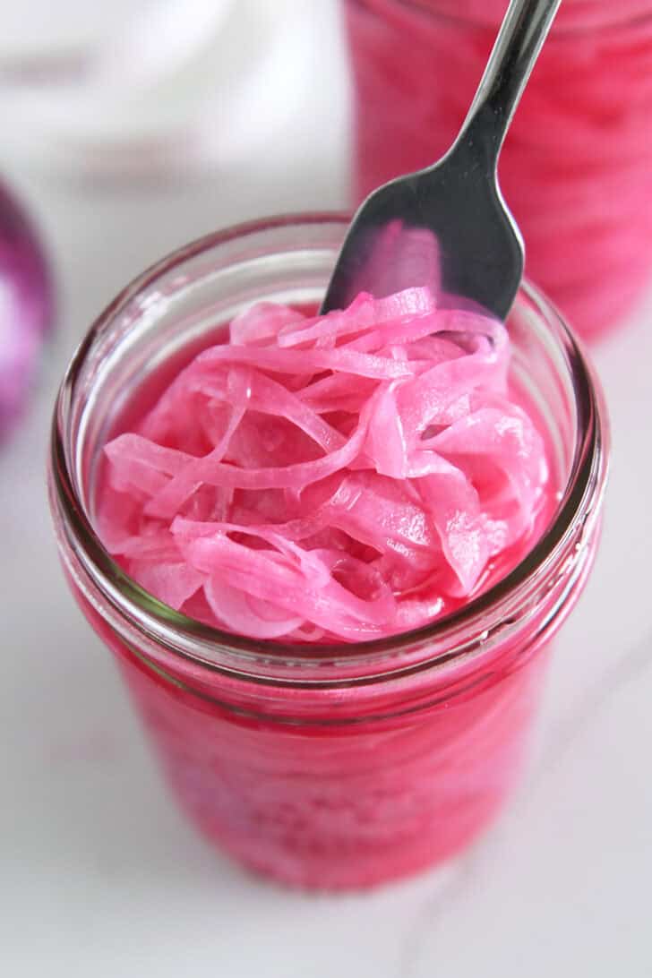 Fork grabbing forkful of thinly sliced pickled red onions.