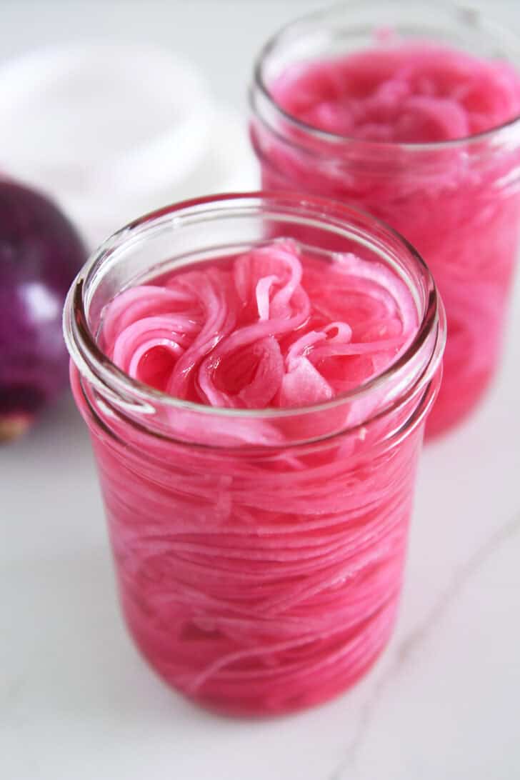 Two pint jars with thinly sliced red onions and vinegar.