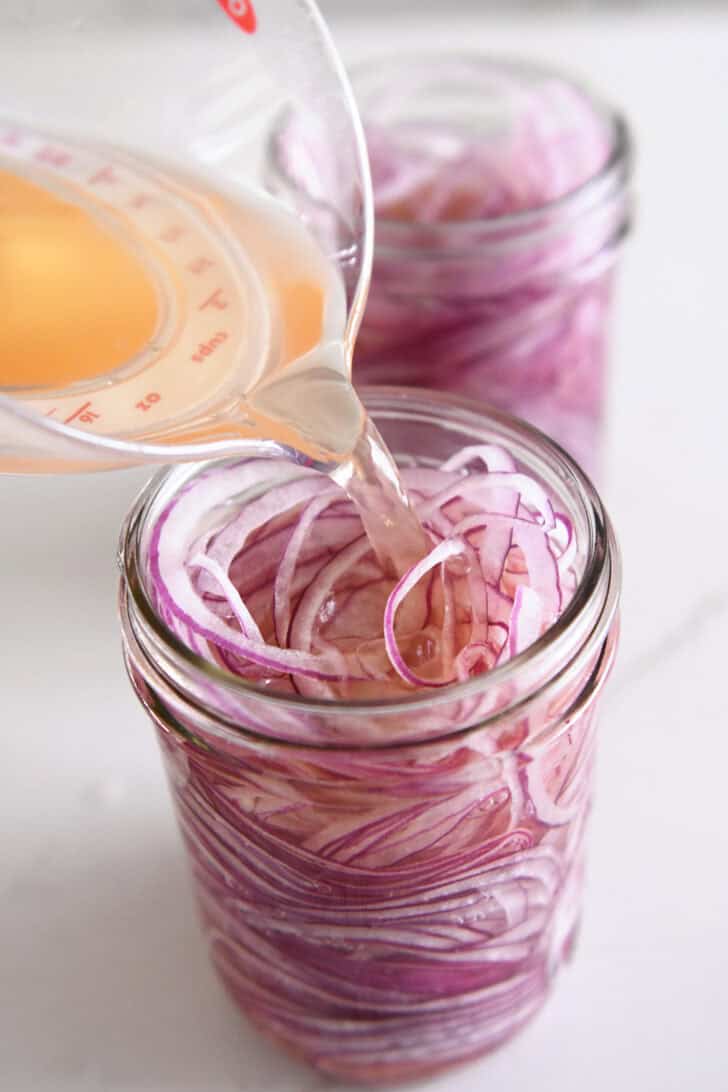 Pouring vinegar, salt and sugar in jar of thinly sliced red onions.