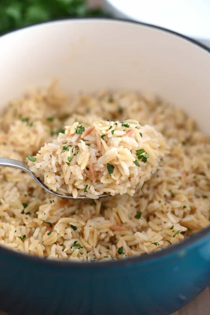 Serving spoon lifting rice pilaf in cast iron pot.