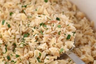 Serving spoon in cast iron pot with rice pilaf and fresh parsley.